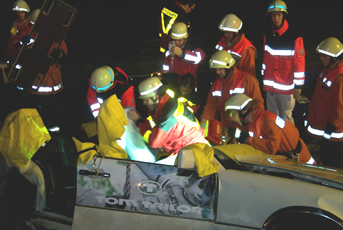 Die Fahrerin wird vom Rettungsdienst und Notarzt betreut während die Feuerwehr die Rückenlehne des Fahrersitzes mit der hydraulischen Schere beseitigt