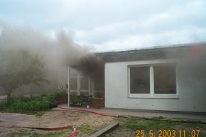 Der erste Löschangriff ist eingeleitet. Ein Atemschutztrupp geht mit einem C-Rohr in den Brandraum vor. Aus der Eingangstür dringt dichter Qualm