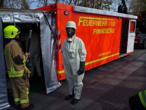 Kamerad vor dem Abrollbehälter Atemschutz/Strahlenschutz in Schutzbekleidung mit den erforderlichen Nachweisgeräten
